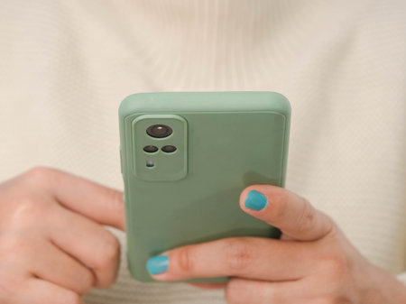 Close-up of female hands holding smartphone. Relaxed young woman in white sweater looking at mobile phone screen enjoying using mobile app for shopping, enjoy playing games at home.の写真素材