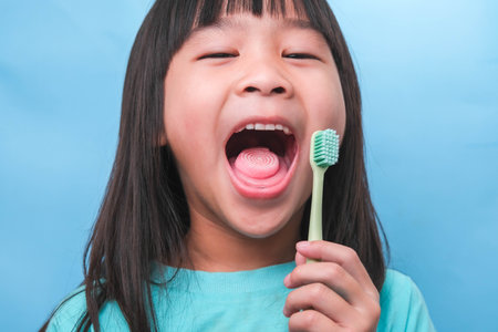 Smiling cute little girl holding toothbrush isolated on blue background. Cute little child brushing teeth. Kid training oral hygiene, Tooth decay prevention or dental care concept.の写真素材