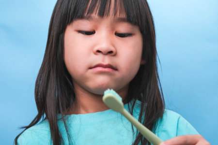Smiling cute little girl holding toothbrush isolated on blue background. Cute little child brushing teeth. Kid training oral hygiene, Tooth decay prevention or dental care concept.の写真素材