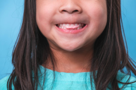 Smiling cute little girl eating sweet gelatin with sugar added isolated on blue background. Children eat sugary sweets, causing loss teeth or tooth decay and unhealthy oral care.の写真素材