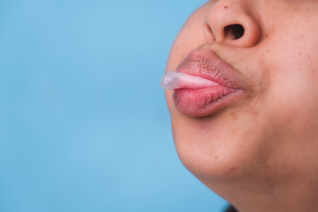 Young woman chewing gum and blowing bubble gum on blue background.の写真素材