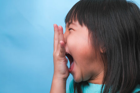 Little asian girl covering her mouth to smell the bad breath. Child girl checking breath with her hands. Oral health problems or dental care concept.の写真素材