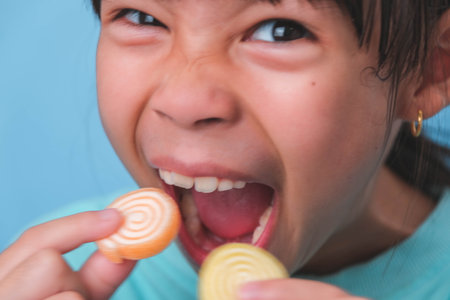 Smiling cute little girl eating sweet gelatin with sugar added isolated on blue background. Children...