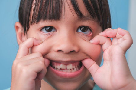Cute little girl making a funny face with her hands on a blue background.の写真素材