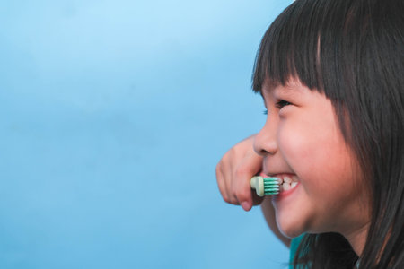 Smiling cute little girl holding toothbrush isolated on blue background. Cute little child brushing teeth. Kid training oral hygiene, Tooth decay prevention or dental care concept.の写真素材