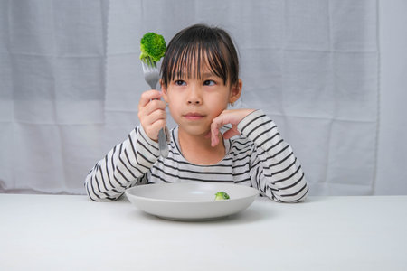Children love to eat vegetables. Cute Asian girl eating healthy vegetables in her meal. Nutrition and healthy eating habits for children.の写真素材