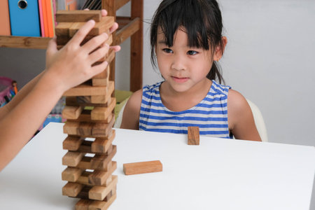 Cute Asian siblings having fun playing together. Two children playing board game on table in room at home. Wooden puzzles are games that increase intelligence for children. Educational toys for children.の写真素材