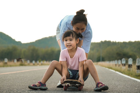 Mother teaching her daughter how to skateboard in the park. Child riding skate board. Healthy sports...