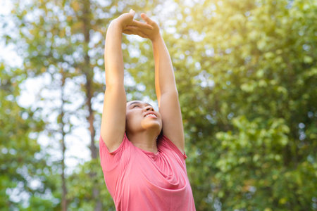 Young Asian woman in sportswear stretches before exercising in the park for a healthy lifestyle. Young healthy woman warming up outdoors. Healthy lifestyle concept.の写真素材