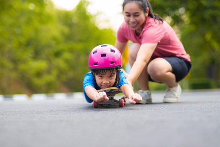 Active little girl and mom enjoy skateboarding. Cute little girl wearing helmet practicing skateboarding in park. Mother trains her daughter to skateboard. Outdoor sports for children.の写真素材