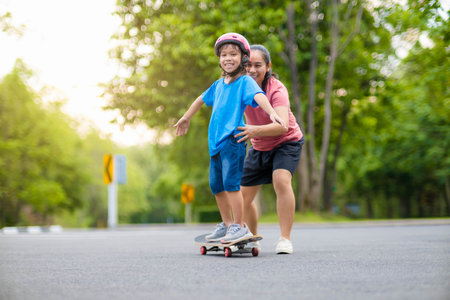 Active little girl and mom enjoy skateboarding. Cute little girl wearing helmet practicing skateboarding in park. Mother trains her daughter to skateboard. Outdoor sports for children.の写真素材