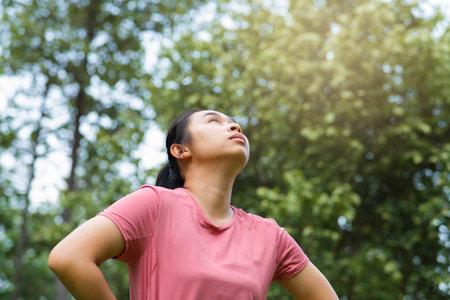 Portrait of young Asian woman in sportswear resting after jogging. Healthy young woman taking a break after jogging in the park. Healthy lifestyle concept.の写真素材