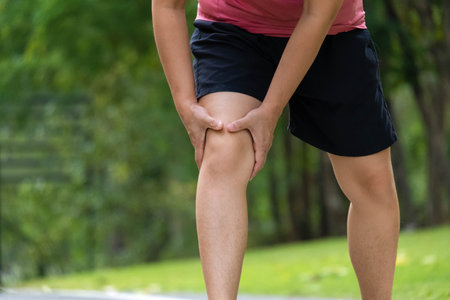 Close-up of young female athlete having knee pain after exercise. Female athlete having leg pain while exercising in park. Exercise injury conceptの写真素材
