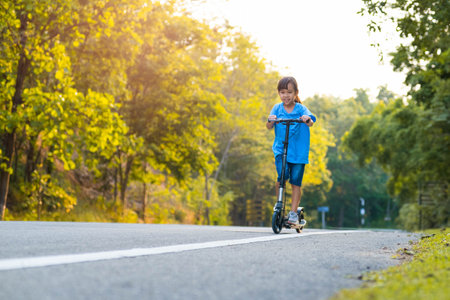 Active little girl riding a scooter on the road in the park on a summer day. Cute little girl wearing helmet enjoys riding kick scooter in outdoor park. Leisure activities and outdoor sports for children.の写真素材