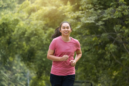 Woman jogging in the park in the sunshine on a beautiful summer day. Beautiful young woman jogging training exercise. Healthy lifestyle concept.の写真素材
