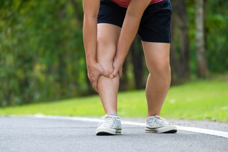 Close-up of young female athlete having knee pain after exercise. Female athlete having leg pain while exercising in park. Exercise injury conceptの写真素材