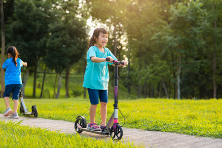 Active little girl riding a scooter on the road in the park on a summer day. Cute little girl wearing helmet enjoys riding kick scooter in outdoor park. Leisure activities and outdoor sports for children.の写真素材
