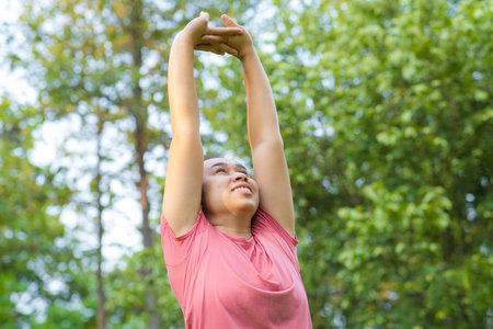 Young Asian woman in sportswear stretches before exercising in the park for a healthy lifestyle. Young healthy woman warming up outdoors. Healthy lifestyle concept.の写真素材