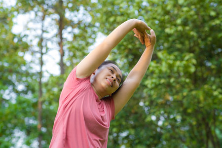 Young Asian woman in sportswear stretches before exercising in the park for a healthy lifestyle. Young healthy woman warming up outdoors. Healthy lifestyle concept.の写真素材