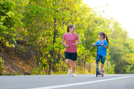 Active little girl riding a scooter on a park road on a summer day with her mother. Outdoor sports for children. Family spending time togetherの写真素材