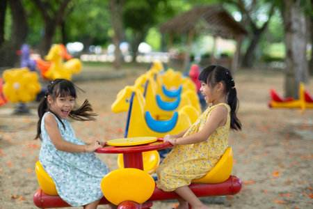 Children sit on a carousel in the playground together. Children playing at outdoor playground in the park on summer vacation. Healthy activity.の写真素材
