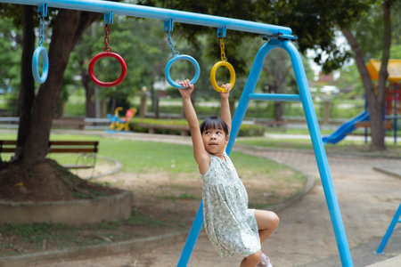 Happy girl hanging on monkey bar by hand doing exercise. Little Asian girl playing at outdoor...