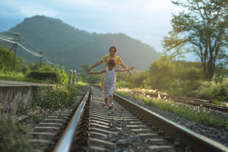 Mother and cute daughter walking on the railroad in the daytime. Happy family walking on the railway against the background of mountains and greenery.の写真素材