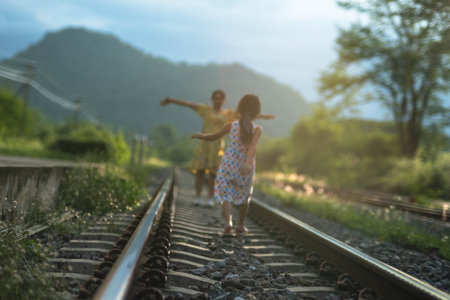 Mother and cute daughter walking on the railroad in the daytime. Happy family walking on the railway against the background of mountains and greenery.の写真素材