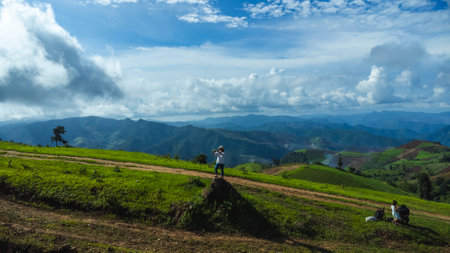 Tourists stand on the rocks enjoying the picturesque hillside views with vast fields on a beautiful sunny day with blue sky and clouds in springtime.の写真素材