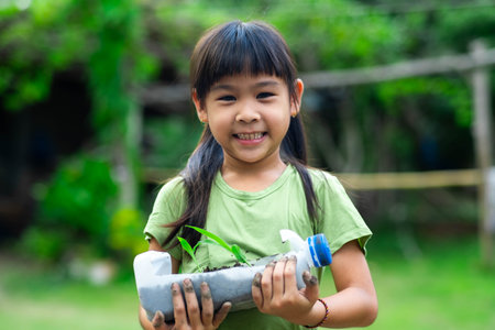Little girl shows saplings grown in recycled plastic bottles. Recycle water bottle pot, gardening activities for children. Recycling of plastic wasteの写真素材