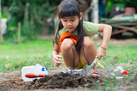 Little girl planting plants in pots from recycled water bottles in the backyard. Recycle water bottle pot, gardening activities for children. Recycling of plastic wasteの写真素材