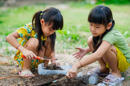 Little girl planting plants in pots from recycled water bottles in the backyard. Recycle water bottle pot, gardening activities for children. Recycling of plastic wasteの写真素材
