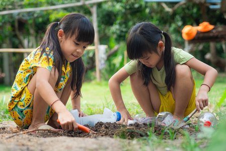 Little girl planting plants in pots from recycled water bottles in the backyard. Recycle water bottle pot, gardening activities for children. Recycling of plastic wasteの写真素材