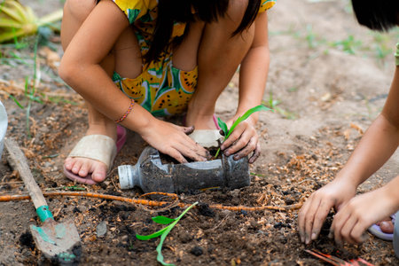 Little girl planting plants in pots from recycled water bottles in the backyard. Recycle water bottle pot, gardening activities for children. Recycling of plastic wasteの写真素材