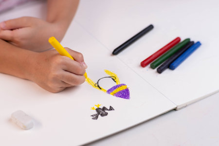 Girl drawing with crayons on a white sheet of paper. Crayons and kids drawing on white background. Close-up of a child's hand holding a crayon and drawing, kids Coloring.の写真素材