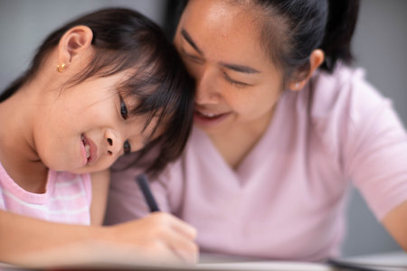 Mother and daughter drawing together with crayons. Adult woman helps girl study or draw together at home in living room. Happy family.の写真素材