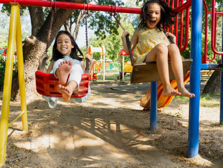 Cute sisters are having fun playing on the swings in a playground in a park. Children playing in the...