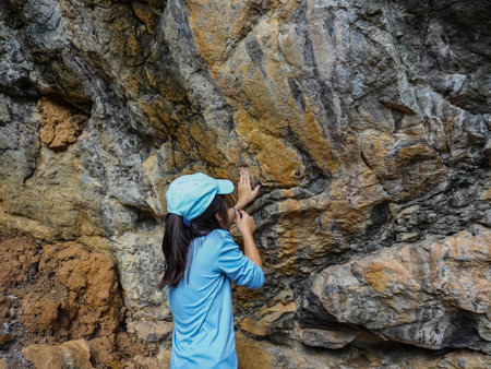 A girl examines rocks through a magnifying glass while exploring the nature of a forest on a sunny day. Outdoor ecology school lesson.の写真素材