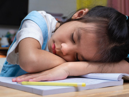 A little school girl is sleeping at her desk. Cute little girl doing homework, sleeping tiredly at home desk.の写真素材