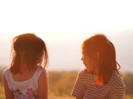 Two little girls are happily playing on meadow during a summer sunset. Family love with colorful sunset.の写真素材