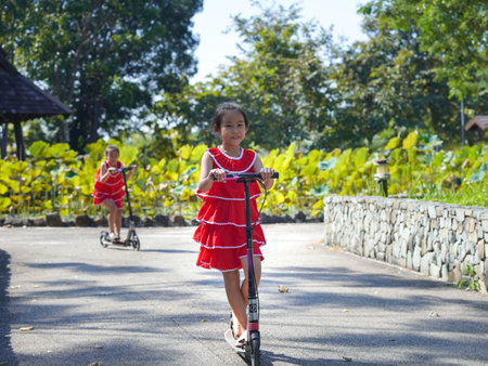 Cute sisters riding scooters on a sunny summer day in the park. Active leisure and outdoor sport for child.の写真素材