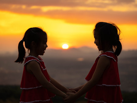 Silhouette of two little girls holding hands on a summer sunset background. Family love with colorful sunset.の写真素材