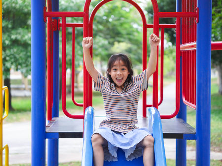 Cute girl playing in the playground during summer vacation. Happy girl having fun on a colorful slide in an outdoor park.の写真素材