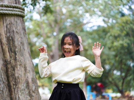 Cute little girl is peeking behind a tree, having fun playing playing peek-a-boo in a sunny garden. Smiling child in the parkの写真素材