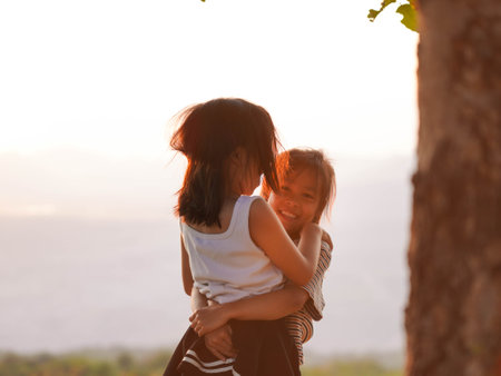Two little girls are happily playing on meadow during a summer sunset. Family love with colorful sunset.の写真素材