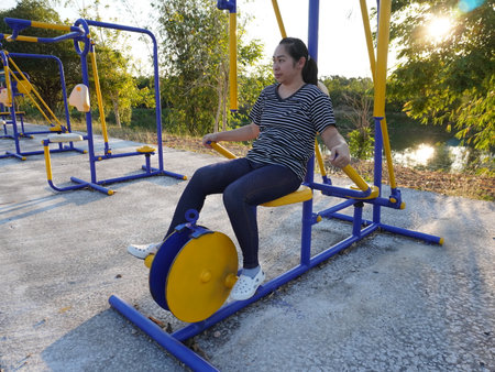Asian adult woman exercising with outdoor fitness equipment in a park.