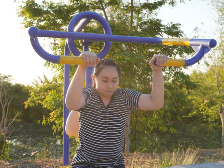 Asian adult woman exercising with outdoor fitness equipment in a park.の写真素材