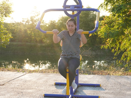 Asian adult woman exercising with outdoor fitness equipment in a park.