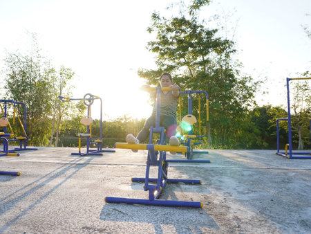 Asian adult woman exercising with outdoor fitness equipment in a park.