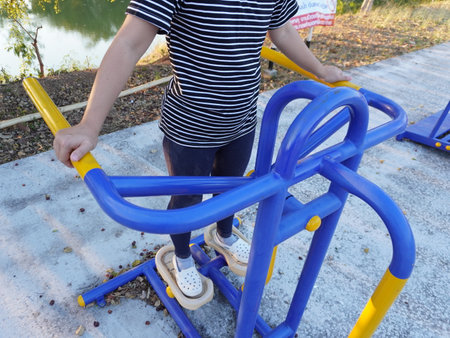 Asian adult woman exercising with outdoor fitness equipment in a park.の写真素材
